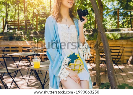 fashion accessories of pretty young stylish woman sitting on vacation in cafe in summer outfit, wearing white dress, blue cape, purse, holding vintage camera