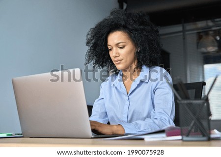 Young serious African American female ceo lawyer businesswoman sitting at desk working typing on laptop computer in contemporary corporation office. Business technologies concept. Royalty-Free Stock Photo #1990075928