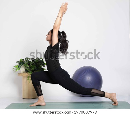 Young attractive smiling woman practicing yoga, wearing sportswear, pants and top, indoor full length at home Royalty-Free Stock Photo #1990087979