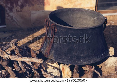 Cooking in sooty old cauldron on campfire at sunny day. Close-up view. Retro toned image.