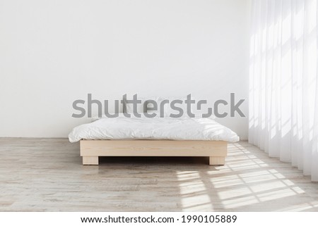 Simple minimalist house design, mockup for ad, blog about interior. Real photo. King size bed on wooden floor in morning light from large window with curtains, on white wall background in bedroom