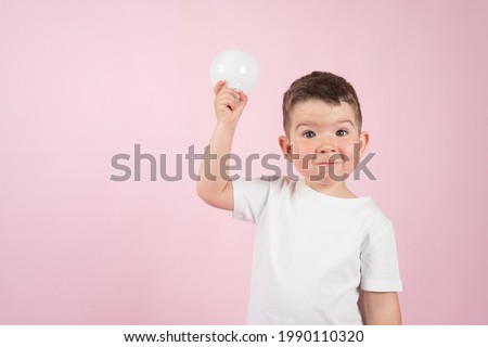 Surprised caucasian boy with light bulb on pink background. High quality photo