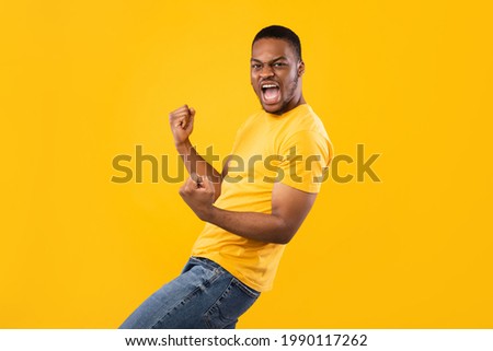 Yes, I Did It. Emotional Black Millennial Man Shaking Fists Celebrating Big Luck And Success Looking At Camera Posing In Studio Over Yellow Background. Victory Celebration, Joy Emotion Concept Royalty-Free Stock Photo #1990117262