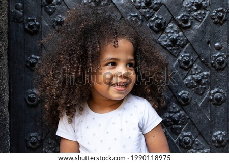 Outdoor portrait of a curly girl on a background of antique black doors.