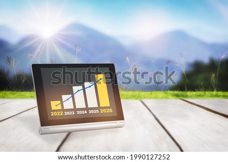 2022 to 2026 sustainable business strategy and financial growth graph stock trading on computer digital tablet on plank and mountain background. Sustainable future energy and smart technology concept