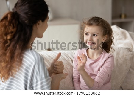 Hispanic mother and small ethnic daughter talk communicate using hand gestures. Cute little teen biracial disabled kid child practice speak with sign language with mom or coach. Nonverbal concept.