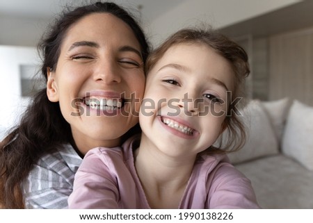 Close up portrait of overjoyed young Latino mother and little biracial daughter make selfie together. Happy Hispanic mom and small ethic girl child take self-portrait picture on camera at home.
