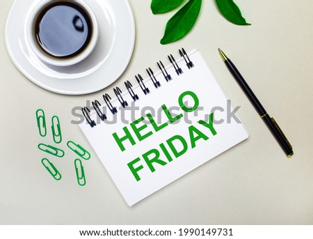 On a light gray background, a white cup of coffee, green paper clips and a green leaf of a plant, as well as a pen and a notebook with the words HELLO FRIDAY.