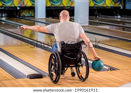 Young disabled man in wheelchair playing bowling in the club