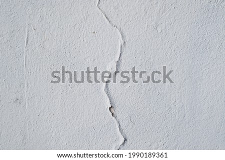 Cracked white paint texture. Crack in the middle of a white rough wall background.