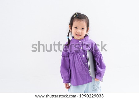 Portrait of a smiling little girl in purple dress holding laptop computer isolated over white background