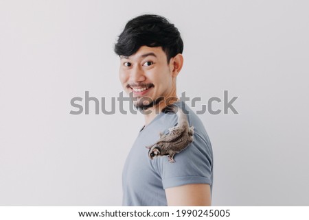 Happy Asian man with his shy Sugar Glider climbing on his body.