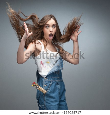 surprised young caucasian female painter with blowing hair over gray background