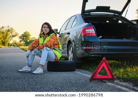 The girl changes the damaged wheel of the car. Green vest. Spare wheel. Traffic accident. Travel by car.