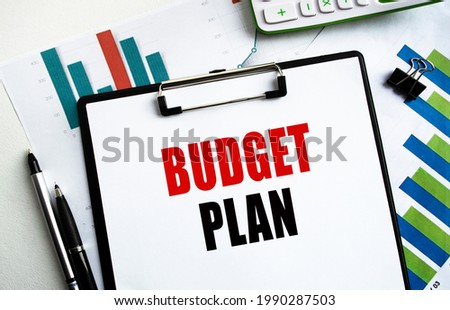 A clip-on folder labeled BUDGET PLAN. Top view of a desktop along with documents, charts and business accessories. Finance or business concept.
