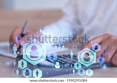 HR specialist researching and analyzing the data of salary on employment market to forecast ongoing expenses of the company using calculator. Hiring new talented officers. Social media hologram icons Royalty-Free Stock Photo #1990295084
