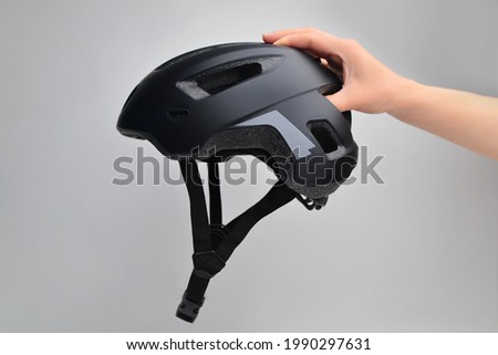 Hand holding bicycle safety helmet for mountain bike or all purpose rider on grey background. This helmet is used to practice cycling. Bike helmet. Black bicycle helmet.  Royalty-Free Stock Photo #1990297631