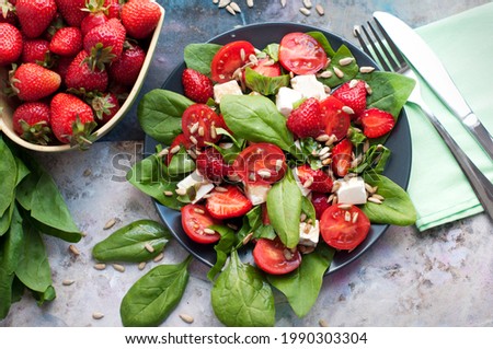 Salad with strawberries, cherry tomatoes, sunflower seeds, spinach and feta cheese on gray background. Top view