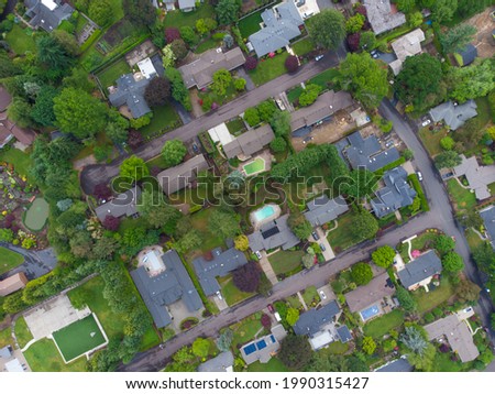 In the photo we see a suburban landscape. In the frame there are roofs of houses, roads, a lot of greenery, trees, bushes, green lawns. High angle view. Aerial photography.