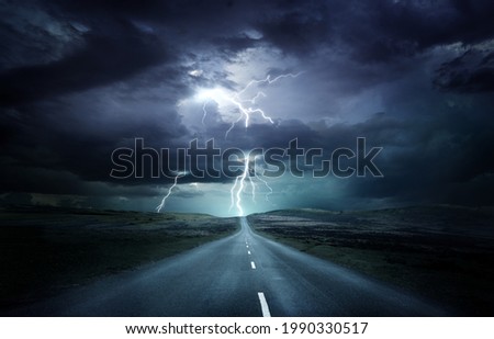 Extreme weather conditions. An empty landscape with a road leading into a powerful thunderstorm with lightning strikes. Photo composition.