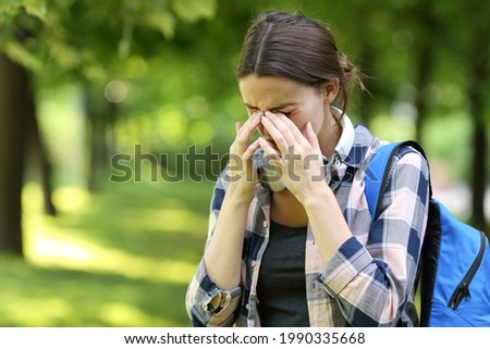 Student suffering allergy symptoms scratching itchy eyes in a park or campus Royalty-Free Stock Photo #1990335668