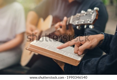 A young boy reads the Bible while his friend plays the guitar. when he worships God A small group of Christians or concepts in a church at a church.
