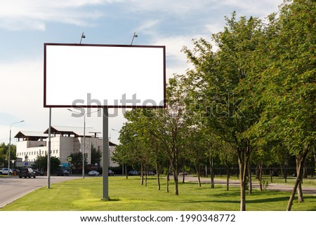 Empty large horizontal billboard on the lawn in the city next to the trees. Mock up.