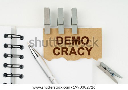 Business and finance concept. On a white background lies a notebook, a pen, clothespins and cardboard with the inscription - Demo Cracy