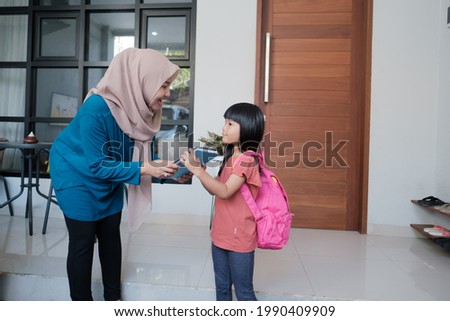 portrait of indonesian primary school female student shake and kiss her muslim mother's hand before going to school