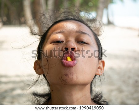 Face of Asian Young Woman with Black Hair Eating a Piece of Mango and Looking at the Camera at Palomino's Beach in La Guajira, Colombia