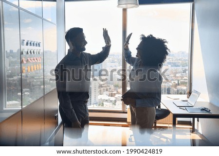 Silhouettes of cheerful successful business partners indian businessman and African American businesswoman colleagues giving high five celebrating business triumph in office at panoramic window. Royalty-Free Stock Photo #1990424819