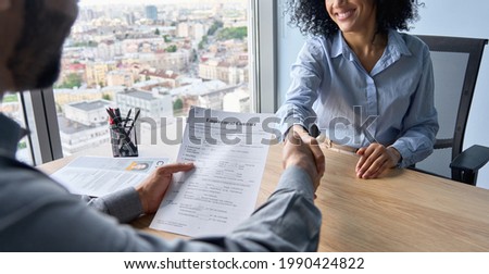 Closeup of Indian employer hr holding employment contract job offer hiring welcoming female African newcomer worker manager shaking hands in contemporary office. Getting new job handshake concept. Royalty-Free Stock Photo #1990424822