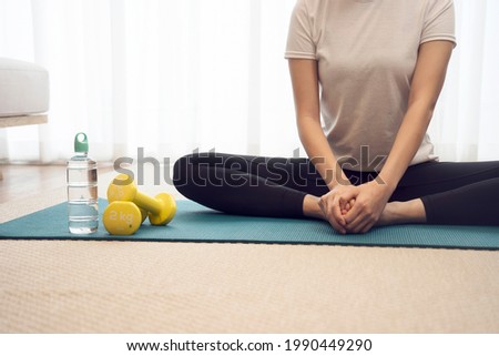 Young woman stretching on a yoga mat to relax or prepare to exercise have  a dumbbell and a water bottle.