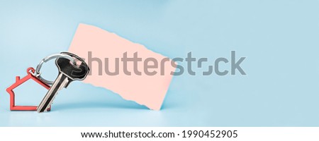 The concept of mortgage, sale and rental of housing and real estate. Keychain in the shape of a house with a key on a light blue background. Paper sticker with place for text. Banner format