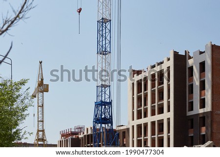In the photo there is a construction of a building next to two cranes.