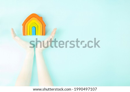 Wooden rainbow house and female hands over light blue background. Selective focus