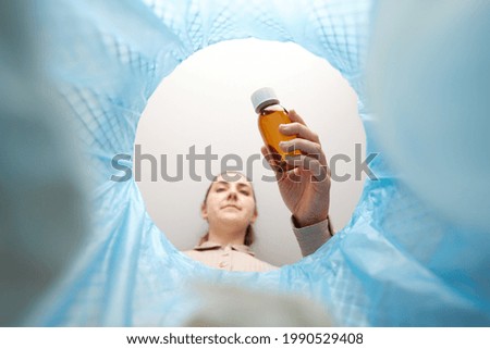 recycling, waste sorting and sustainability concept - woman throwing glass bottle with expired medicine into trash can Royalty-Free Stock Photo #1990529408