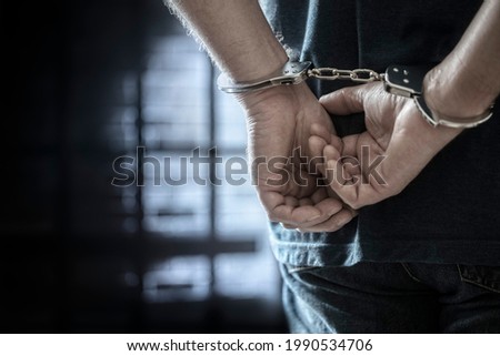 Arrested man in handcuffs with handcuffed hands behind back in prison Royalty-Free Stock Photo #1990534706