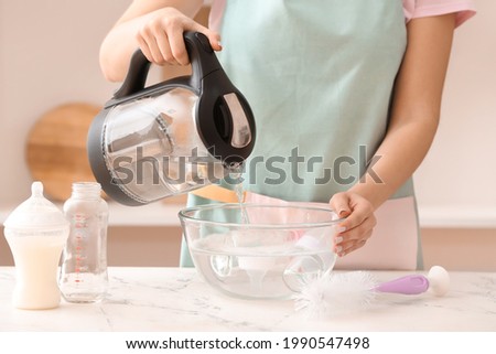 Woman cleaning baby bottle at home Royalty-Free Stock Photo #1990547498
