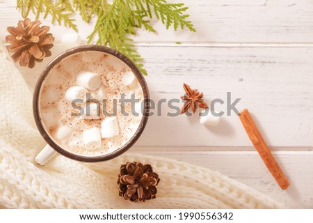 hot chocolate mug with marshmallows, cone, cinnamon sticks, white sweater, fir branches on a white wooden background, top view