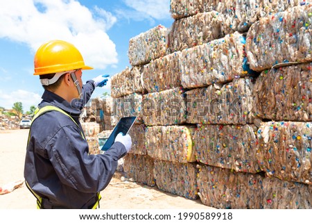 An employee at a recycling plant is pointing to plastic waste being sent to the recycling process. Engineer looking and pointing forward. Royalty-Free Stock Photo #1990589918