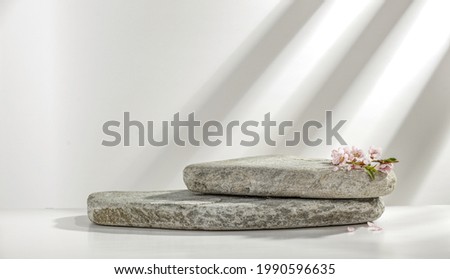 White background with stone and fresh flowers. Wall with shadows and free space for your product. 
