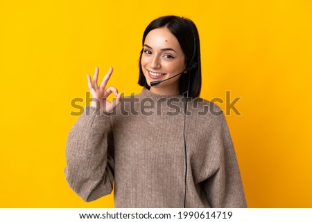 Young telemarketer woman isolated on yellow background showing ok sign with fingers Royalty-Free Stock Photo #1990614719