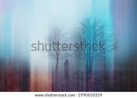 A double exposure of a spooky half transparent hooded figure. Over layered over an abstract, artistic, retro edit. On a moody foggy winters day in the countryside. Malvern Hills, UK