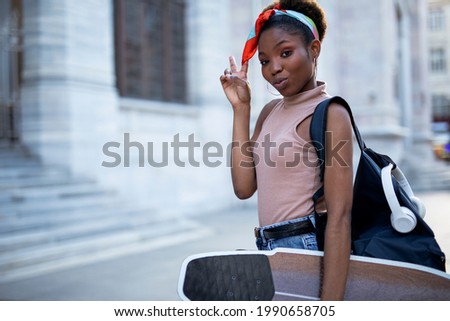 Portrait of happy african-american woman with a skateboard. Young stylish woman with skateboard outdoors.