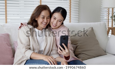 Candid attractive beautiful two people asia young lady girl use mobile phone take photo picture video overjoy sit at home sofa couch have good time day together quarantine in mum healthy health care.