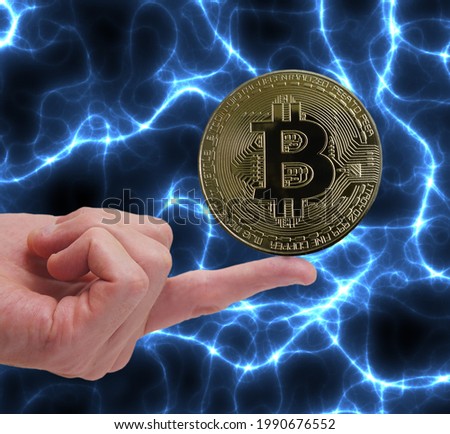 Bitcoin cryptocurrency coin balancing on a finger with blue energy background