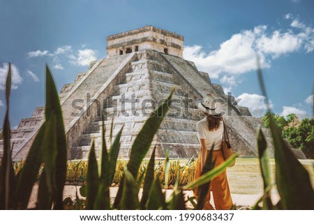 A young woman tourist in a hat stands against the background of the pyramid of Kukulcan in the ancient Mexican city of Chichen Itza. Travel concept.Mayan pyramids in Yucatan, Mexico  Royalty-Free Stock Photo #1990683437