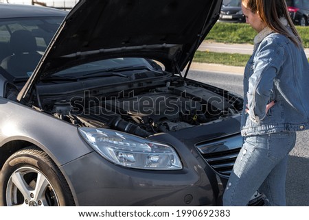 Car problem. Driver girl near open hood auto after accident triangle on road. Vehicle broken down or motor car engine problem concept