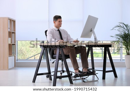 Man using footrest while working on computer in office Royalty-Free Stock Photo #1990715432